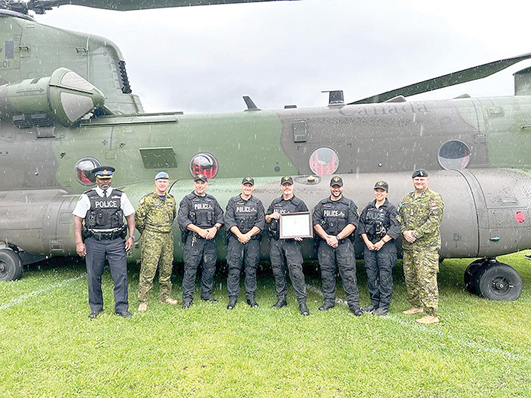 Eight people stand in a row in front of Chinook helicopter, one in middle hols framed item